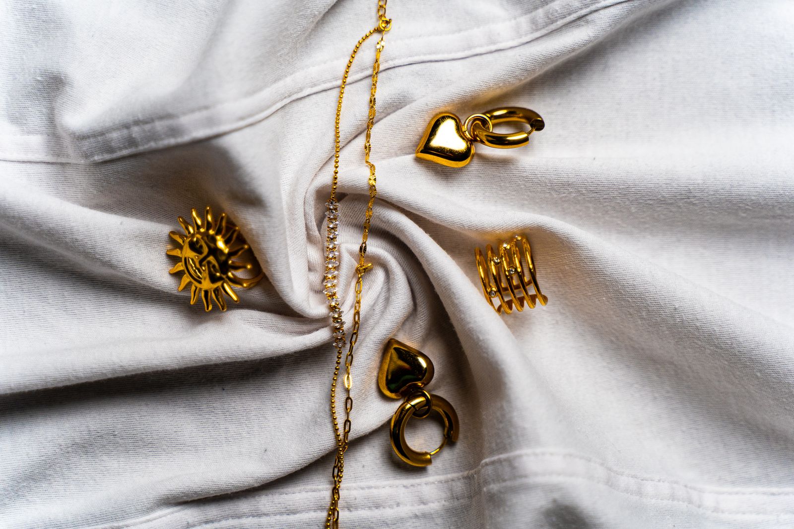 Gouden ringen, oorbellen en kettingen op witte zijde